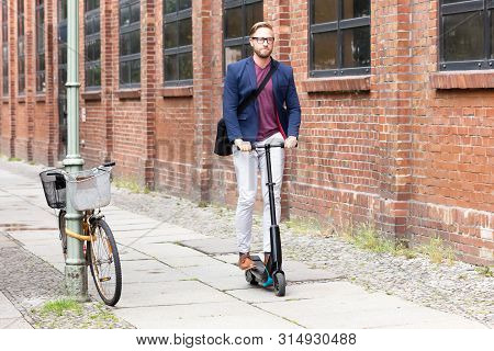 A Young Businessman With Shoulder Bag Riding An Electric Scooter On Street