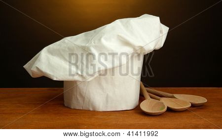 Chef's hat med skedar på bordet på brun bakgrund