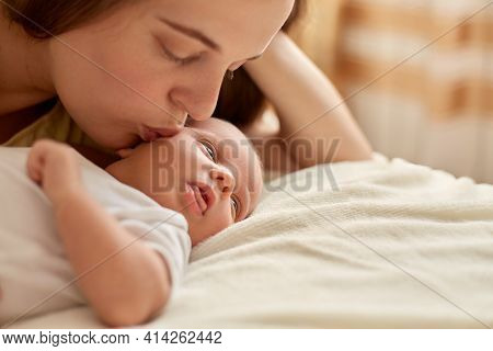 Mother And Her Newborn Baby Together Lying On Bed On Blanket. Happy Mother Kissing And Hugging Baby,