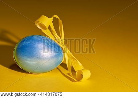 Pearl Colored Egg With Yellow Ribbon On A Yellow Background. Easter Concept.