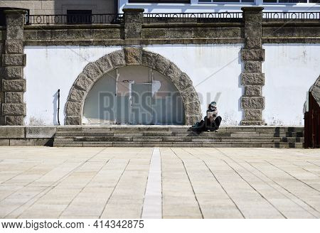 La Coruña (spain), March 22, 2021. A Woman Reads In The Sun Sitting On A Stone Bench. Due To The Cor
