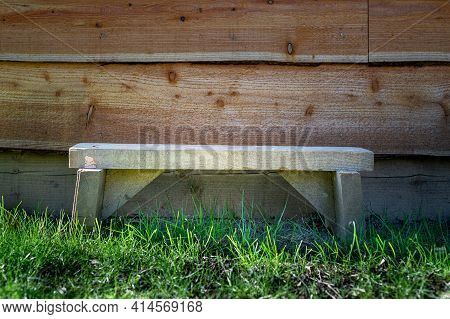 Small Wooden Hand Made Bench Sits On Grass In Front Of Waney Edge Wooden Garden Shed.