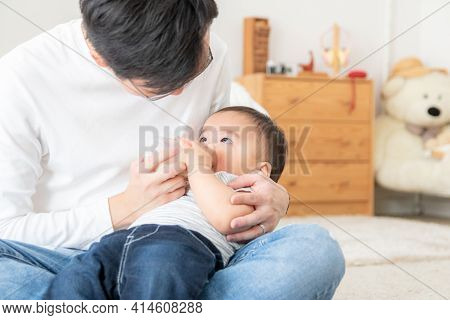 Portrait Of An Asian Father Feeding A Baby With Milk In A Bottle. Happy Family Concept
