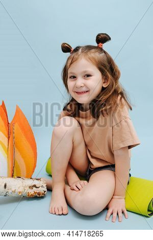 Portrait Of Smiling Little Girl Sitting Next To A Fake Campfire Over Blue