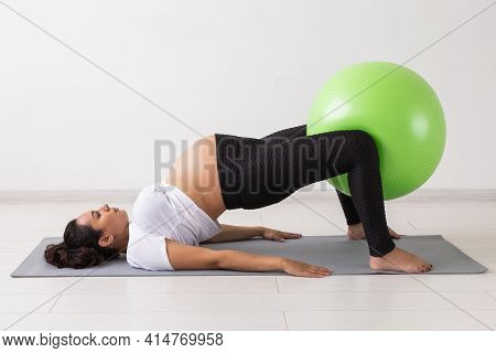 Young Flexible Pregnant Woman Doing Gymnastics On Rug On The Floor On White Background. The Concept 