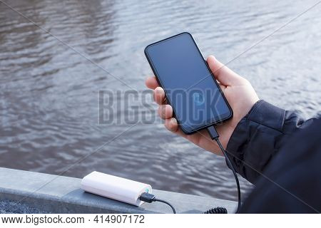 A Man Charges A Smartphone With A Power Bank. The Phone In Hand Is Being Charged With A Portable Cha