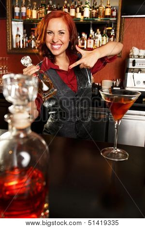 Beautiful redhead barmaid with bottle behind bar counter 