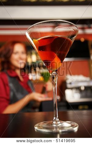 Cheerful barmaid with cocktail behind bar counter 