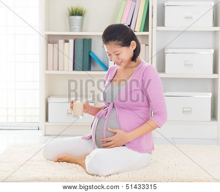 Asian 8 months pregnant woman enjoying a glass of soymilk as breakfast,  relaxing at home. 