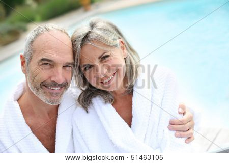 Happy senior couple in bathrobe by resort pool