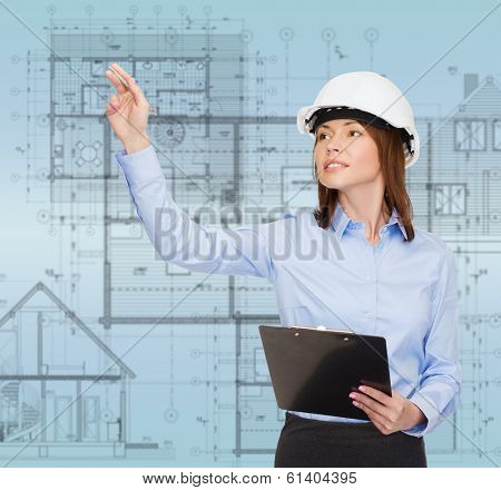 building, developing, consrtuction and architecture concept - smiling businesswoman in white helmet with clipboard pointing finger