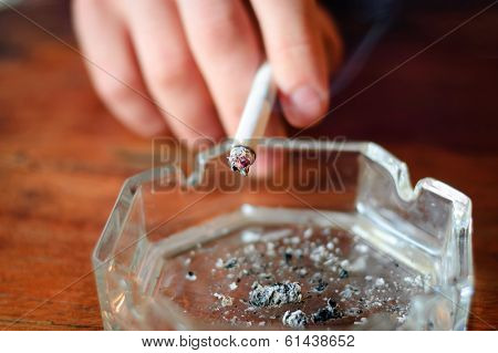 hand with cigarette and ashtray. selective focus at end of cigarette and ash.