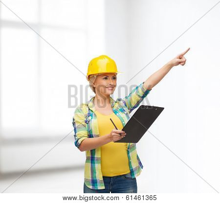repair, construction and maintenance concept - smiling woman in helmet with clipboard pointing finger