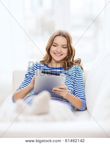 home, technology and internet concept - smiling teenge girl lying on the couch with tablet pc computer at home