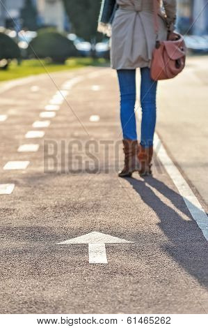 Close-up of woman legs walking on bike alley and arrow sign