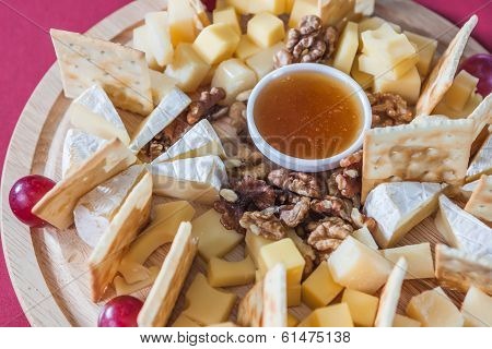 Different Varieties Of Cheese With Grapes, Crackers, Nuts And Honey On Wooden Plate