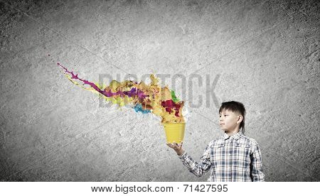 Young boy splashing colorful paint from bucket