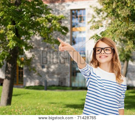 education, school and imaginary screen concept - cute little girl in eyeglasses pointing in the air or imaginary screen