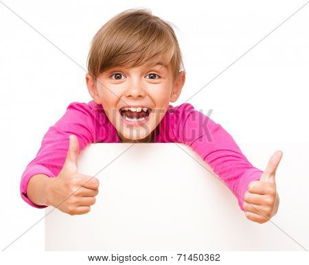 Little girl is looking out from the blank banner showing thumb up sign, isolated over white