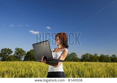 Mladá žena na poli pšenice s notebookem