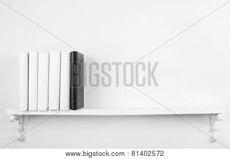 Blank books with black one on bookshelf on white wall background