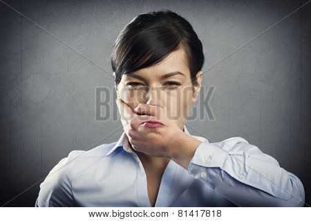 Angry upset businesswoman with hand covering her mouth, isolated on grey background.
