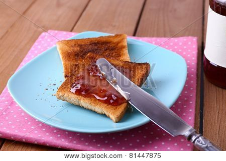 Toast bread spread with jam on plate and napkin with knife near jar on wooden table background