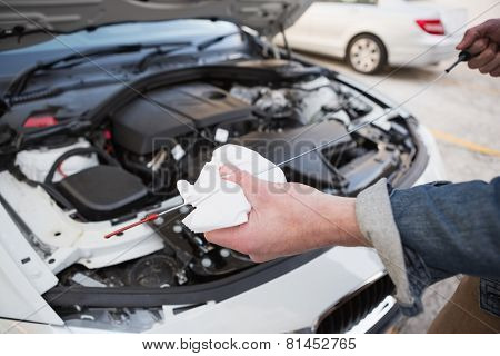 Close up of man checking car engine oil in a car park