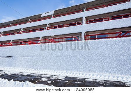concrete modernist building with snow-covered wall against a bright cloudy sky