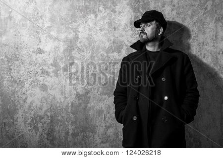 man in vintage cap and coat standing near old wall. black and white photo