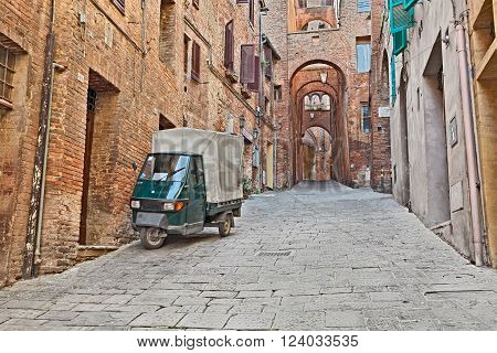 SIENA ITALY - MARCH 22: picturesque Italian alley in the old town with ancient dwellings, archs, and three-wheeled vehicle Ape Piaggio, on March 22, 2016 in Siena, Tuscany, Italy