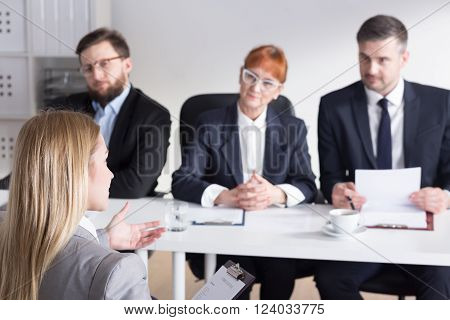 Young pretty intern talking with three bossy businesspeople to work in company