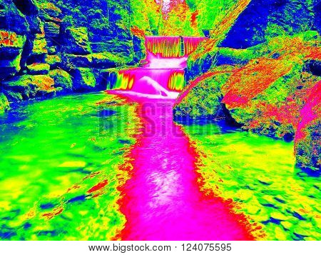 Mossy boulder and water level in shadows of trees. Cold water of mountain river in infrared photo. Amazing thermography.