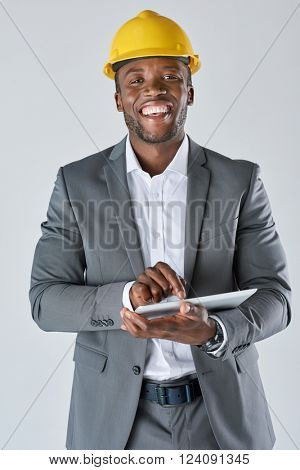 Smiling portrait of black architect engineer designer with touchscreen tablet device in business suit isolated in studio
