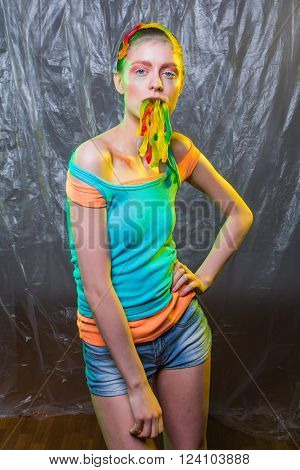 Young woman with colorful make up holds gummy jelly worms candies in mouth.