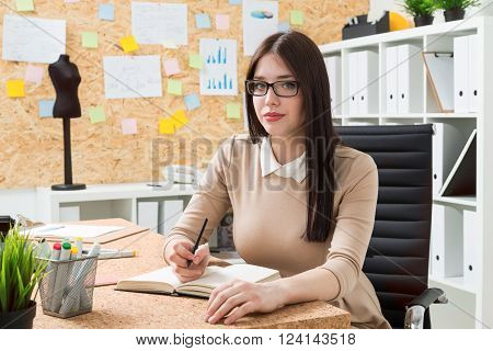 Woman in glasses making notes tailor dummy at background. Office. Concept of work.