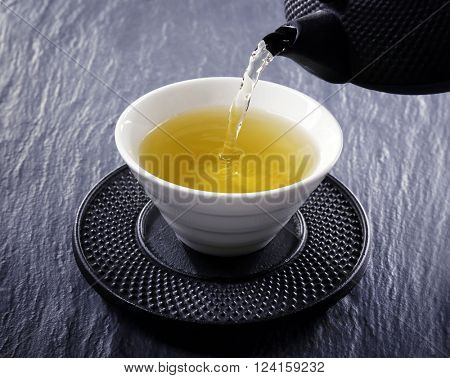 Pouring green tea into white pialat on slate plate background