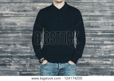 Caucasian man in black shirt and jeans standing in front of wooden wall. Mock up
