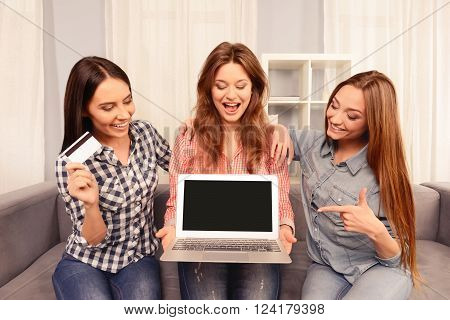 Three Girls Sitting On Sofa And Showing Black Screen Of Laptop And Bank Card