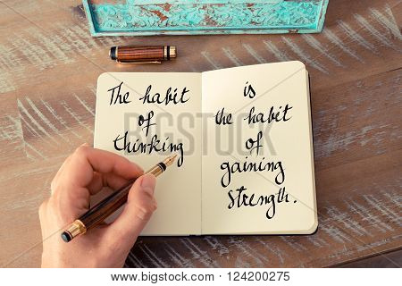 Retro effect and toned image of a woman hand writing on a notebook. Handwritten quote The habit of thinking is the habit of gaining strength as inspirational concept image