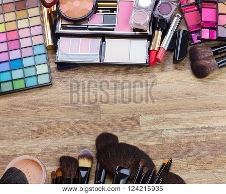 brushes, lipsticks, maskara, eye shadows and  powder on wood, top view with copy space