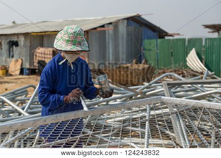 Petchaburi, Thailand - February 20, 2016: One woman worker paints wire metal fence in silver color at prepared area of outdoor construction on February 20, 2016 in Petchaburi, Thailand