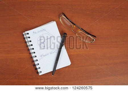 ballpoint pen glasses and an open notebook lying on the table