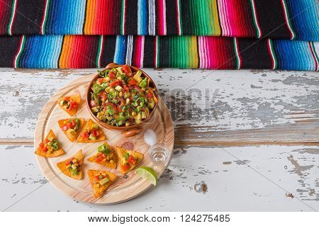 Nachos chips and vegetables in an earthenware bowl tequila lime salt and poncho seen from above