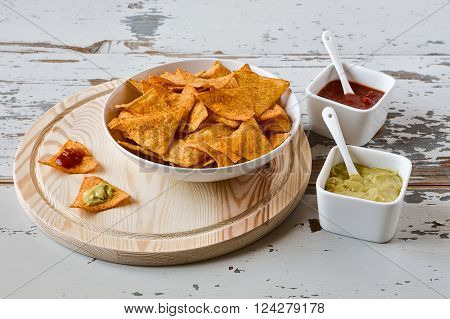 Nachos chips with sauce on a chopping board on a wood background