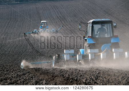 Blue tractor with sower on the field in bright sunny spring morning
