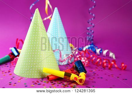 Two Birthday hats with serpentine streamer and noise makers on purple background