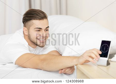 Beautiful young man waking up with mobile alarm clock