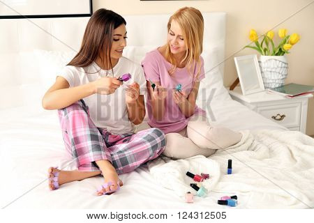 Two girls painting toenails on a bed in living room