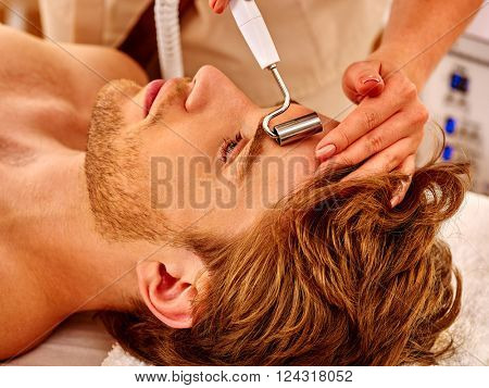 Man gets rejuvenating electric galvanic face spa massage at beauty salon. 